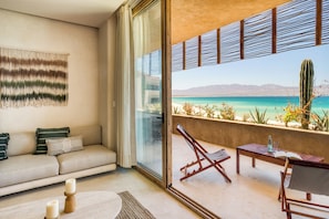 Una sala de estar moderna con un sofá, una mesa de centro y un balcón con vistas a una playa y cactus.