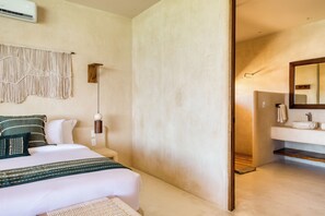 A bedroom with a bed, bedside table, wall-mounted air conditioner, and a hanging macrame wall decoration. - Amina Wind Resort (La Ventana)