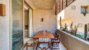 Un balcón con una mesa y sillas de madera, un ventanal de vidrio y un jardín de cactus.