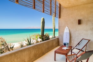 A balcony with a view of the ocean, a surfboard, a table, and a chair. - Amina Wind Resort (La Ventana)
