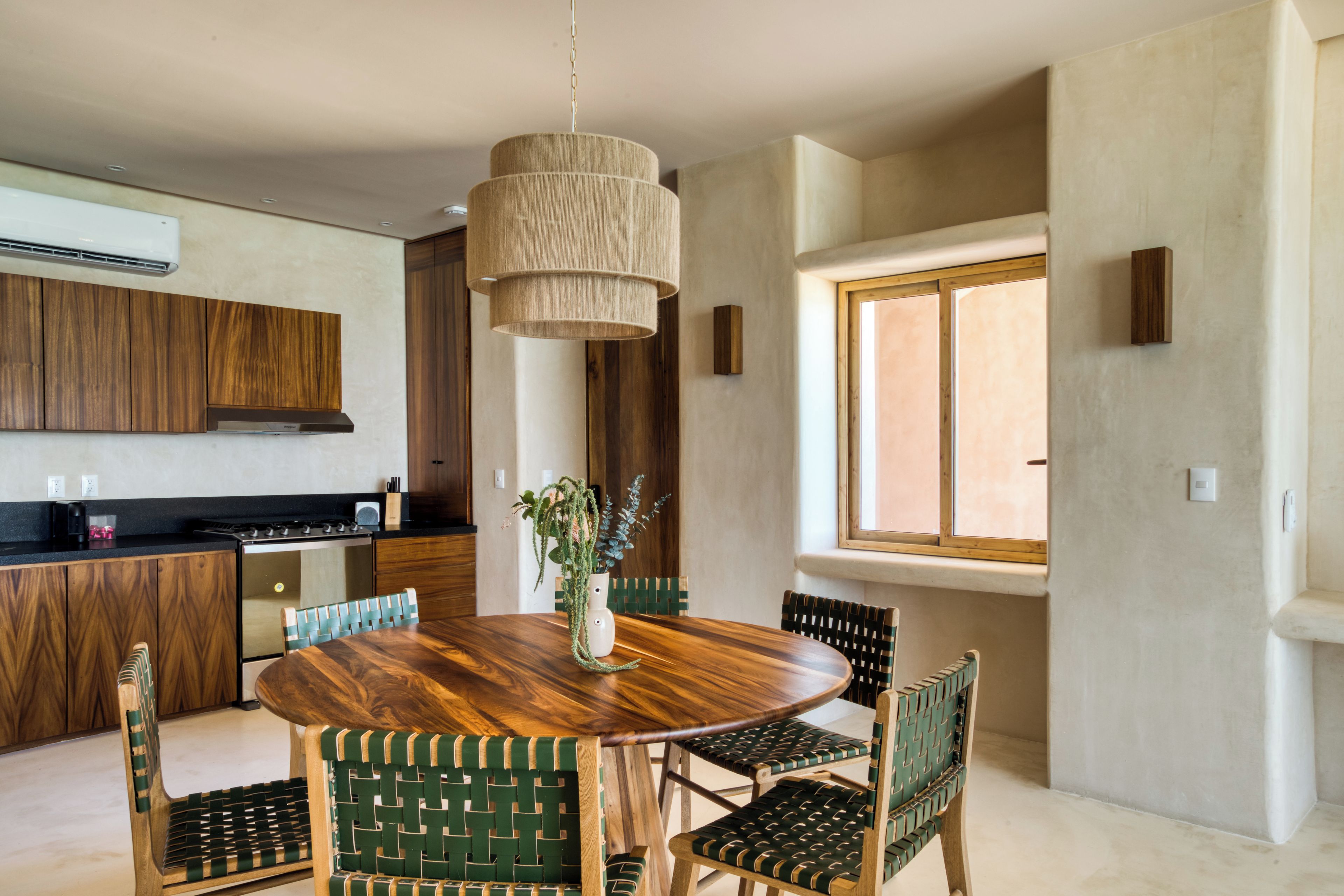 Een moderne keuken met houten kastjes, een ronde eettafel en groene geweven stoelen.