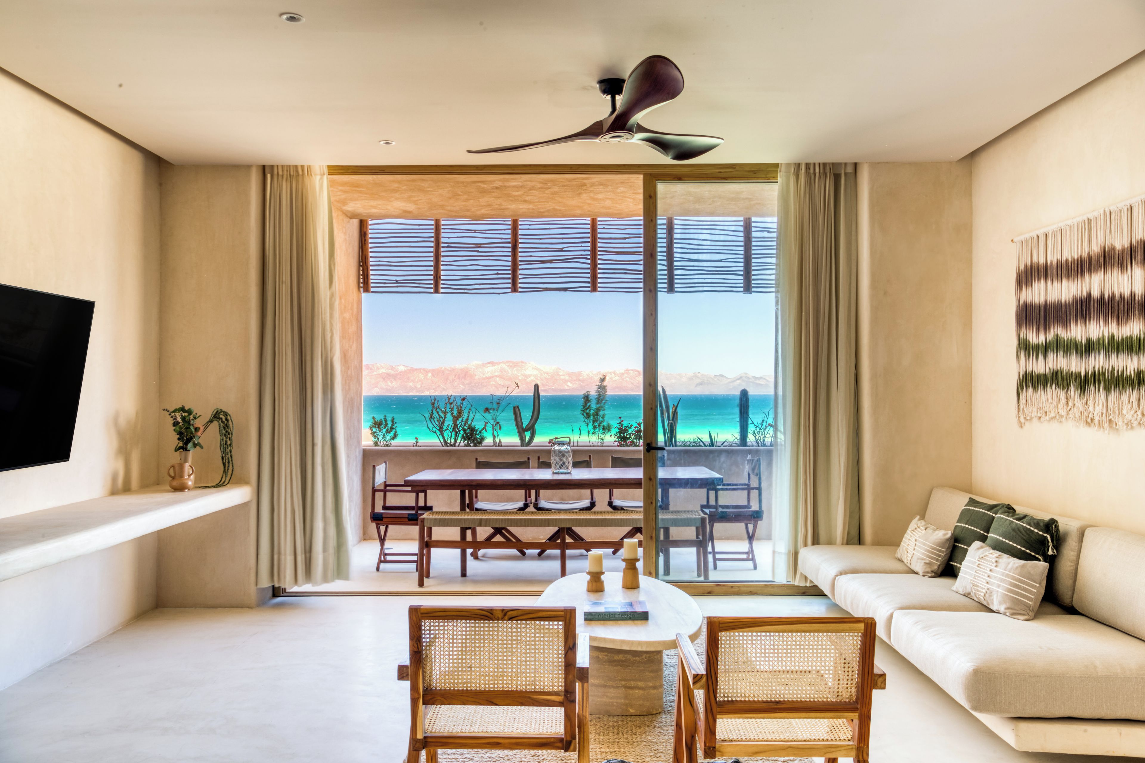 Una sala de estar moderna con comedor, ventanas grandes con vista al océano y un ventilador de techo.