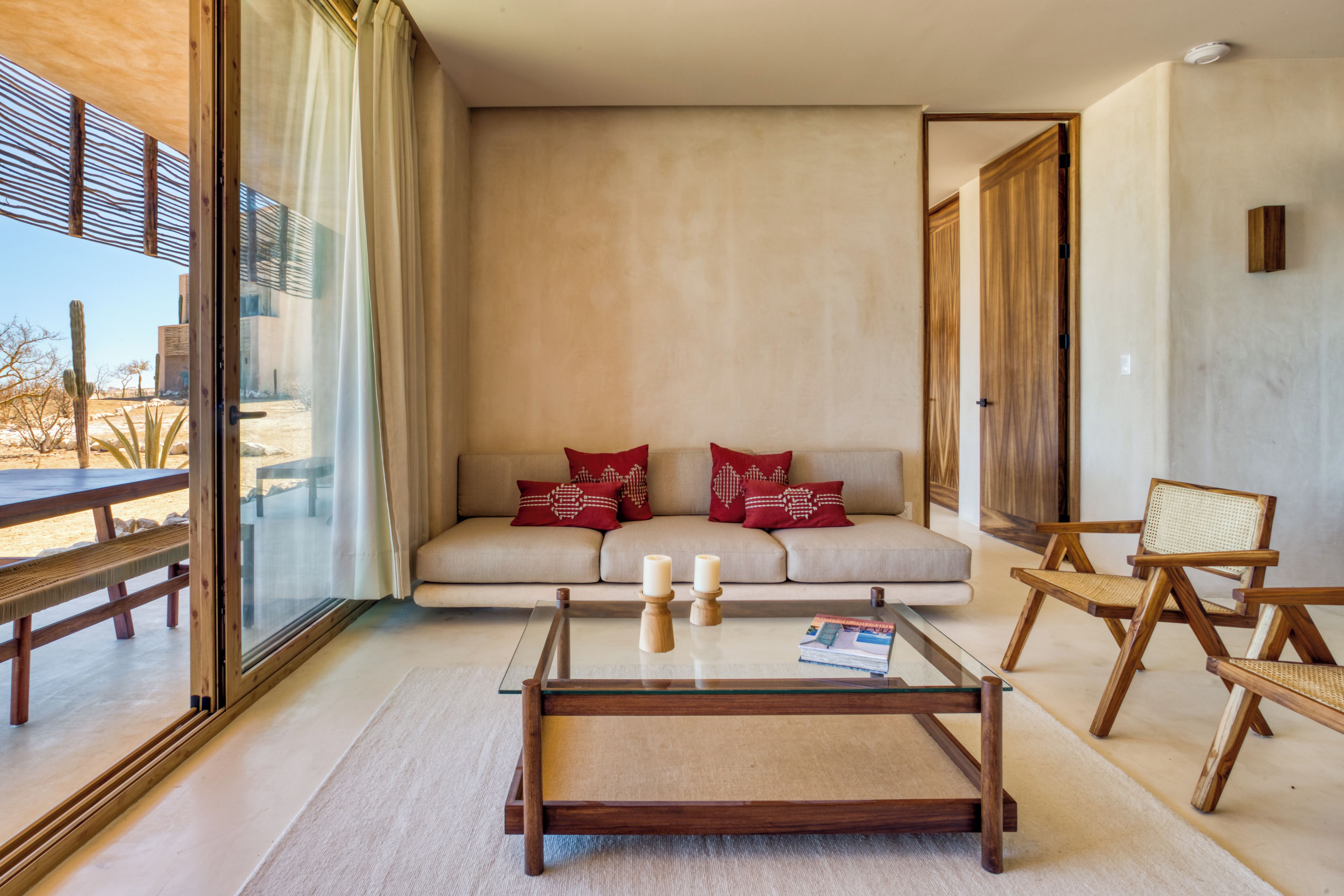 A modern living room with a glass coffee table, a sofa with red cushions, and wooden chairs.