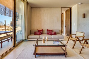 A modern living room with a glass coffee table, a sofa with red cushions, and wooden chairs. - Amina Wind Resort (La Ventana)
