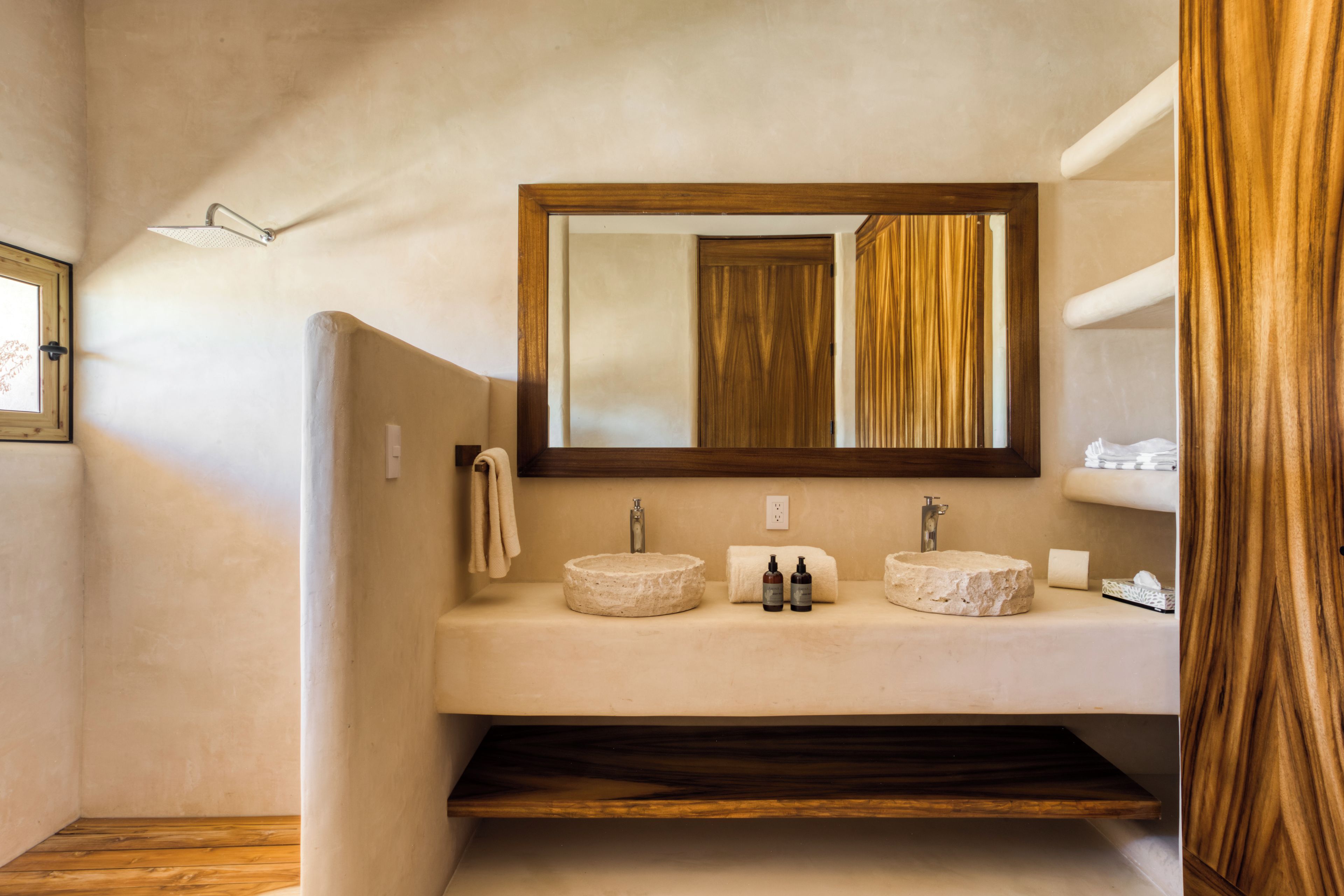 Un baño con un lavamanos redondo, dos espejos y estantes de madera.