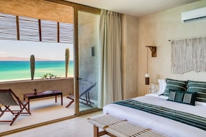 Un dormitorio con cama, un banco, una mesa, una silla, vistas al océano y un balcón.