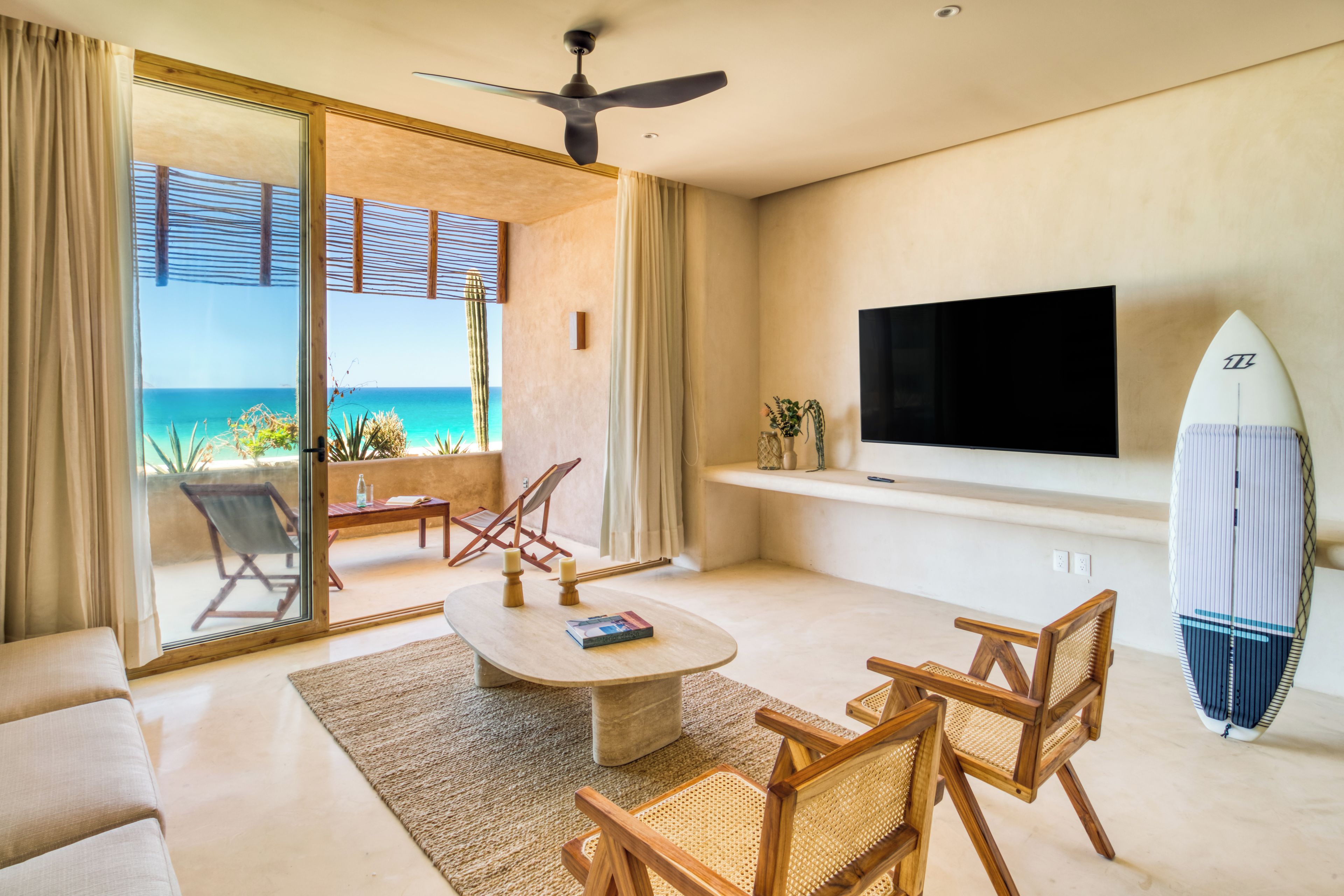 Ein modernes Wohnzimmer mit großem Fernseher, einem Surfbrett und Blick auf den Ozean.