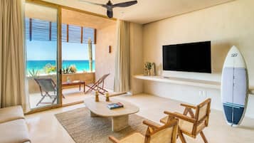 Ein modernes Wohnzimmer mit großem Fernseher, einem Surfbrett und Blick auf den Ozean.