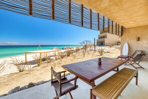 A beachside dining area with a wooden table and chairs, a bench, and a view of the ocean. - Amina Wind Resort (La Ventana)