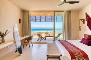 A bedroom with a bed, a bench, a surfboard, a desk, and a chair.
