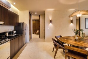 A modern kitchen with dark wood cabinets, stainless steel appliances, and a marble countertop. There is a dining area with a wooden table and chairs, and a pendant light above. - Amina Wind Resort (La Ventana)