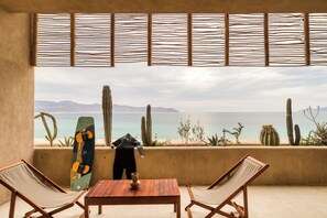 Un balcón con una mesa de madera, dos sillas, un monopatín y un cactus.