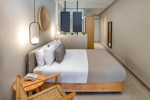 A modern bedroom with a bed, bedside table, chair, and a small table with a phone. - Callia Retreat Suites (Santorini)