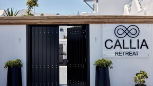 Ein schwarzes Tor mit einem Schild, das 'CALLIA RETREAT' zeigt, und je einer Kübelpflanze auf jeder Seite.