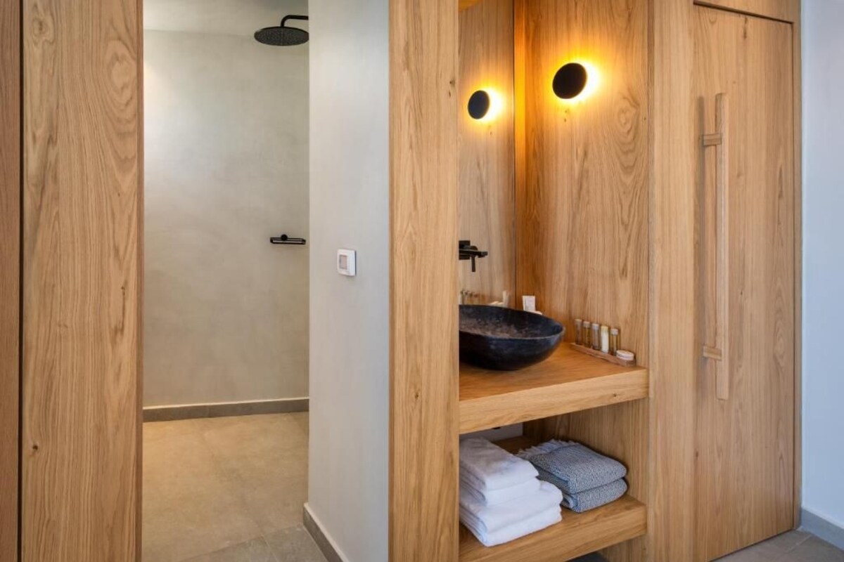 A wooden vanity with a black basin, two wall-mounted lights, and a shelf with towels.