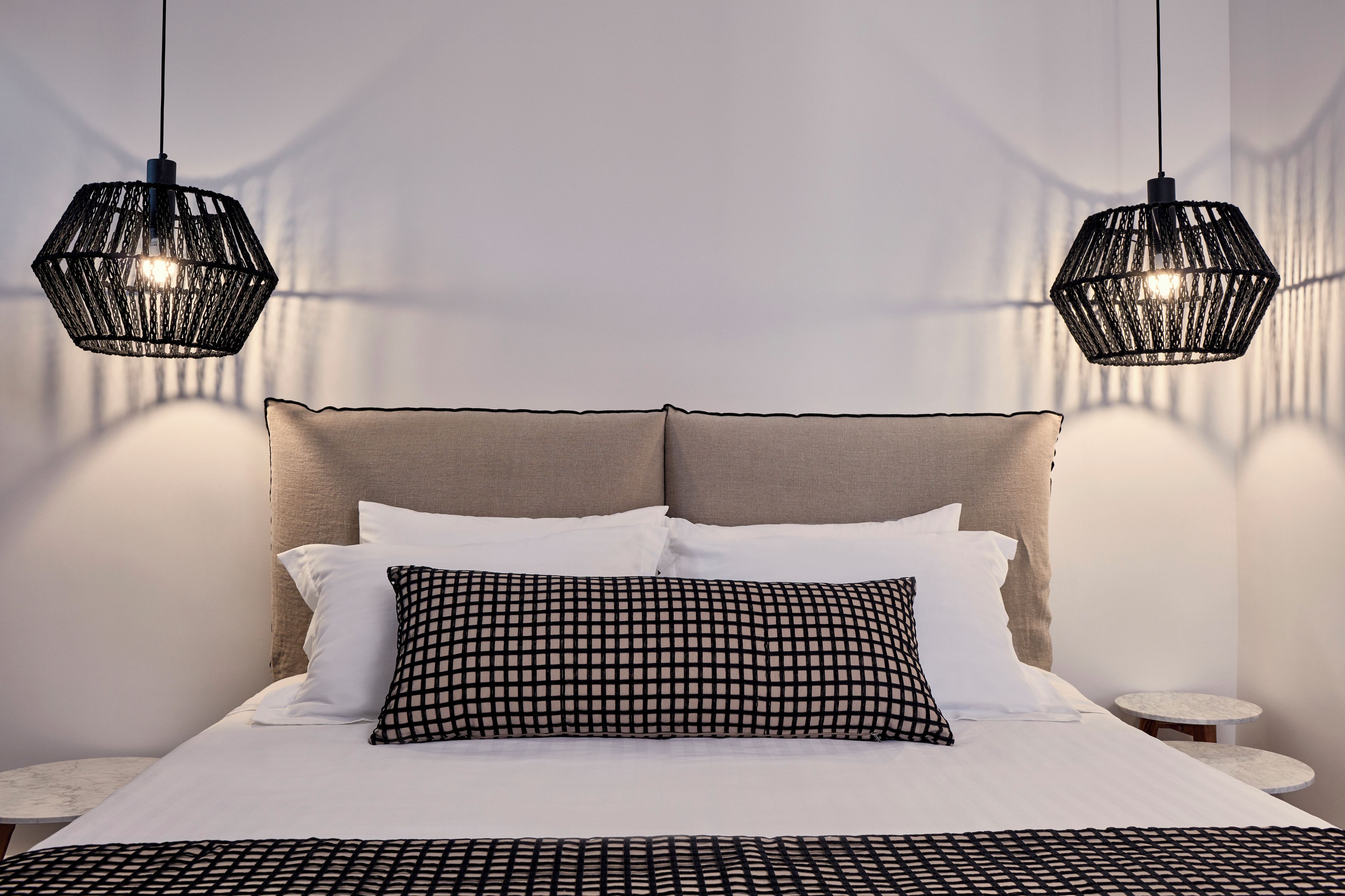 A bed with a headboard, two hanging lights, and a bedside table.