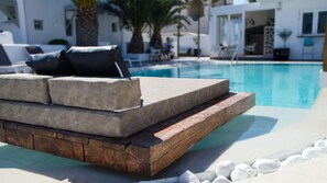 A poolside seating area with a built-in bench and cushions, a wooden deck, and a clear view of the pool. - Callia Retreat Suites (Santorini)