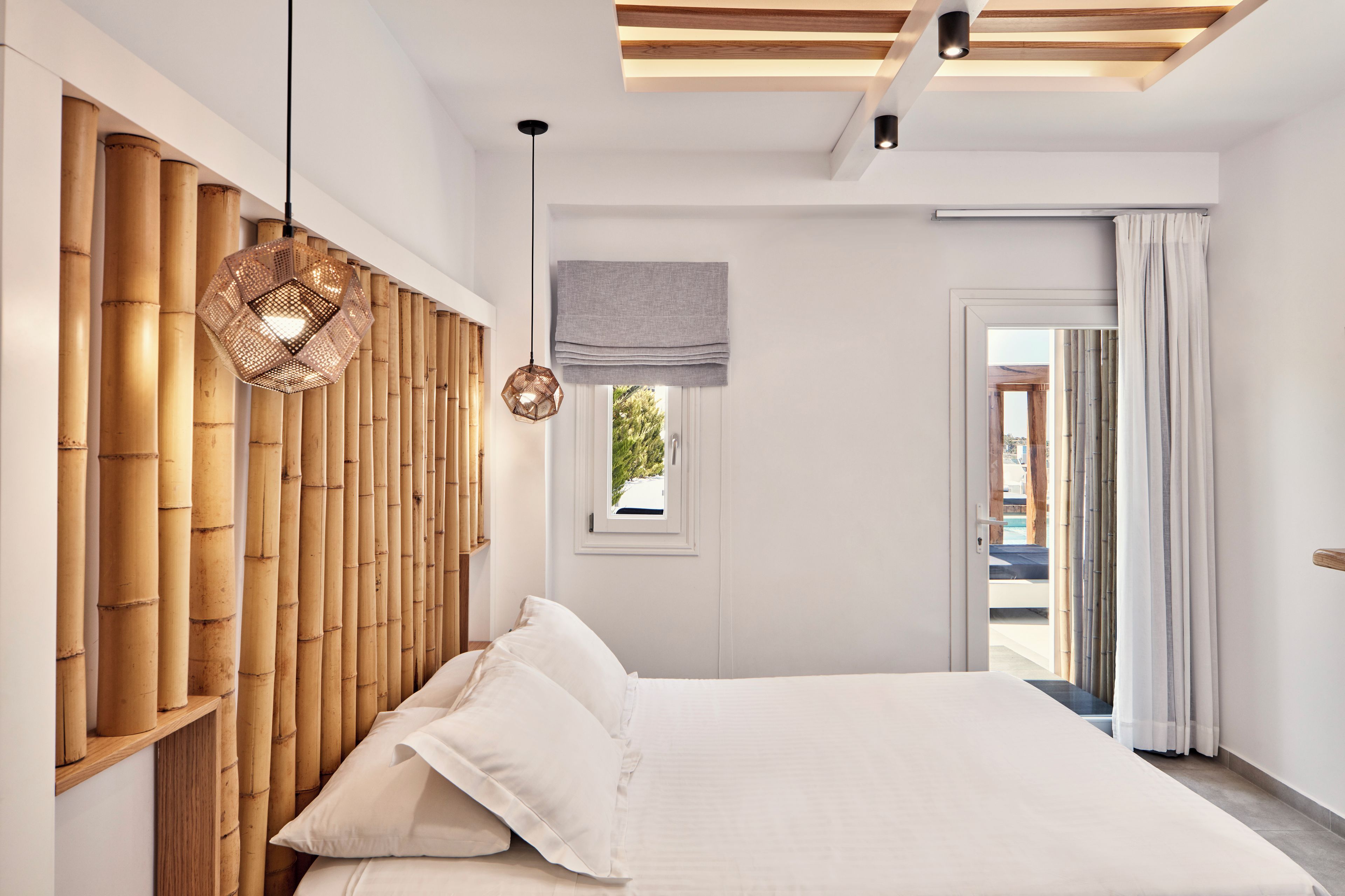 A modern bedroom with a large bed, bamboo headboard, and a view through an open door.