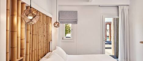 A modern bedroom with a large bed, bamboo headboard, and a view through an open door.