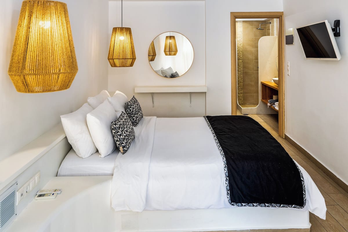 Um quarto moderno com uma cama curva, duas luminárias pendentes, um espelho redondo e uma TV na parede.