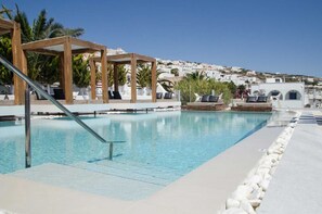 A pool with a wooden pergola, lounge chairs, and a clear view of a hillside town. - Callia Retreat Suites (Santorini)