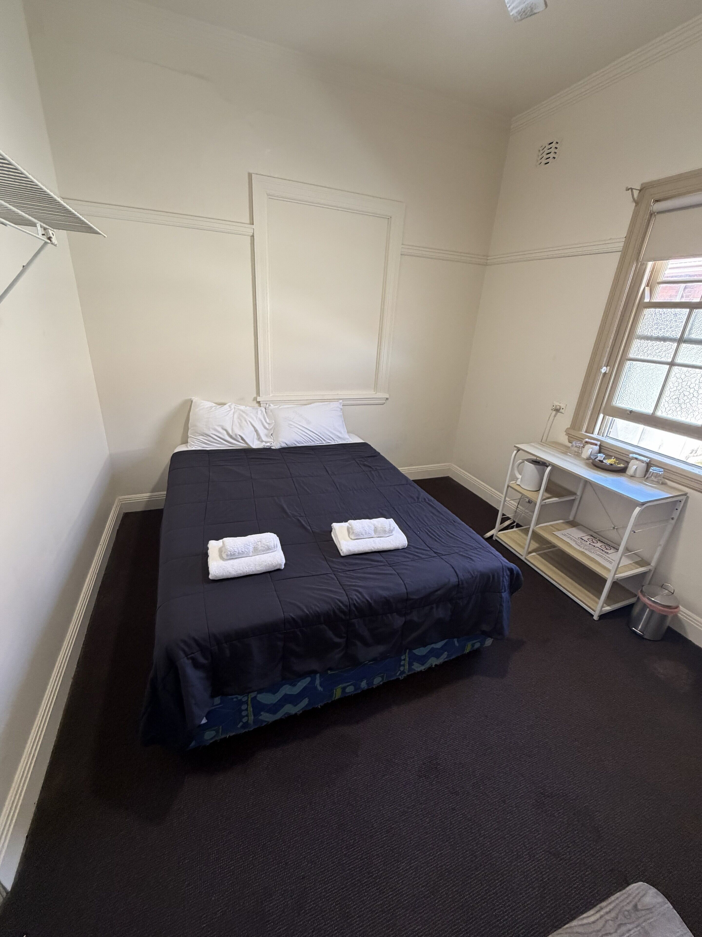 A hotel room with a bed, a small desk with a chair, a window, and a radiator.