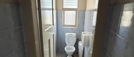 A narrow bathroom with a toilet, a small window, and a tiled floor.