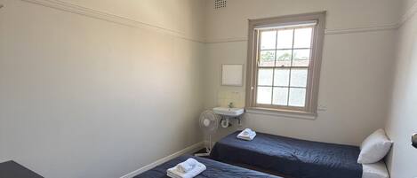 Een slaapkamer met twee bedden, een bureau, een stoel, een raam en een plafondventilator.