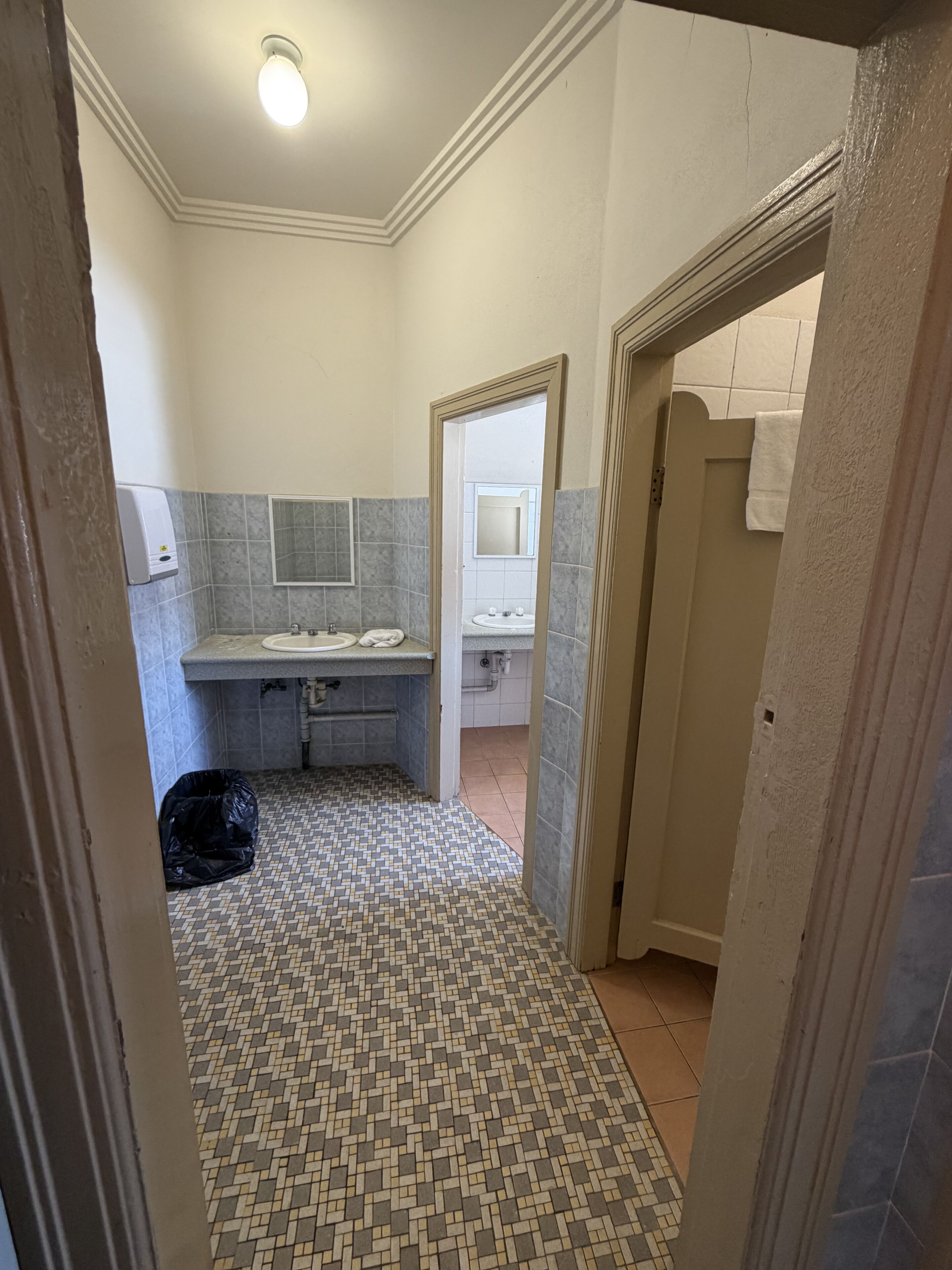 Un baño con piso de baldosas, un lavamanos, un espejo y un perchero para toallas.