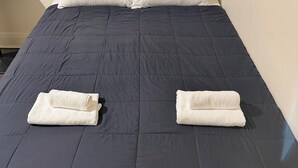 A bed with a dark blue bedspread, two neatly folded white towels, and a white pillow.