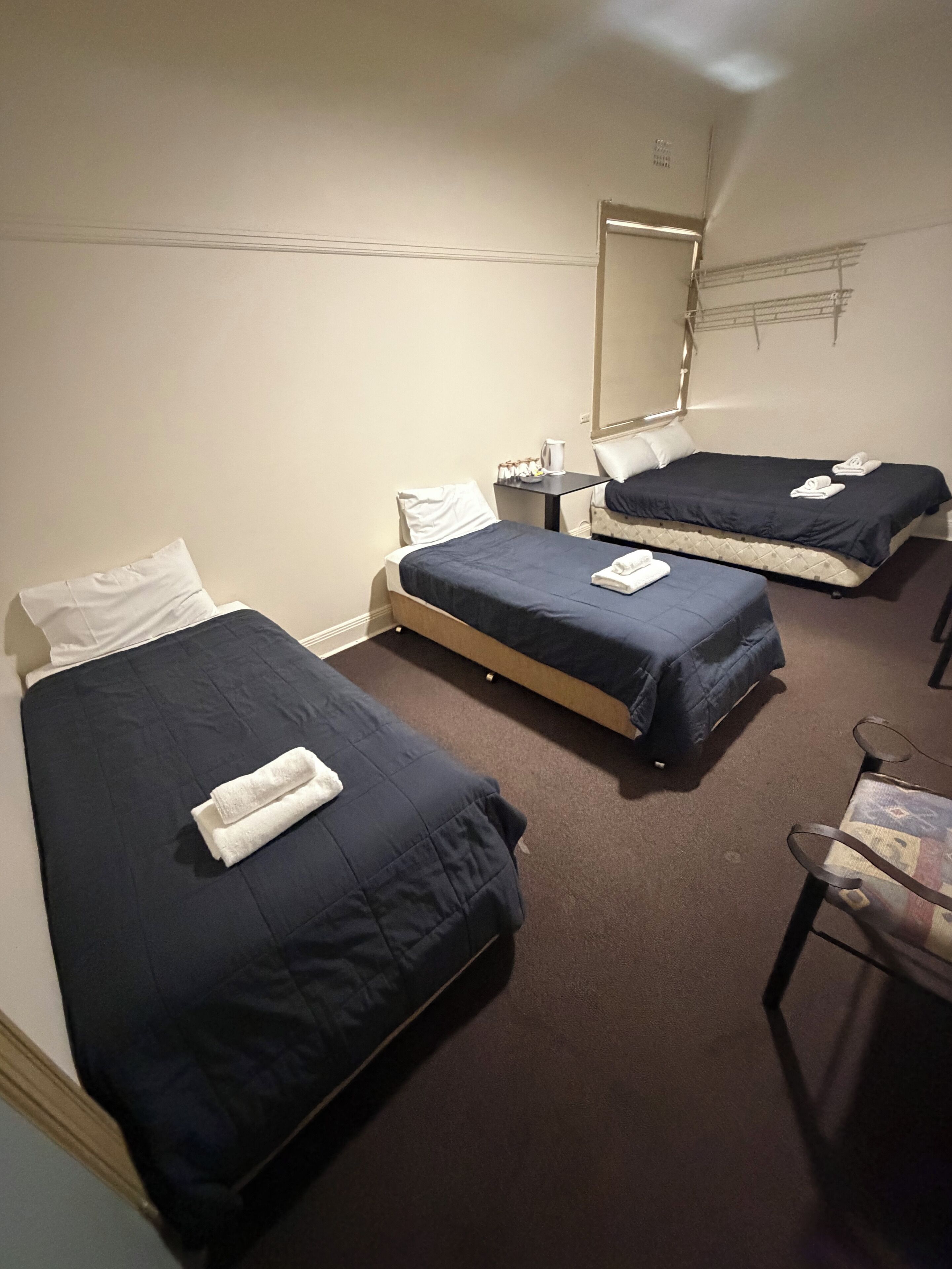 Habitación de hotel con dos camas individuales, una mesita con una tetera y una silla.