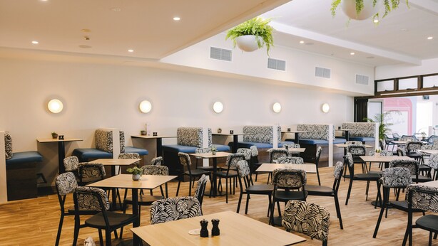 A restaurant with booths and tables, patterned chairs, and hanging plants.