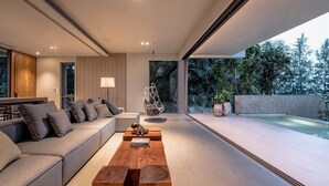A modern living room with a sofa, coffee table, and hanging chair. There is a pool visible outside. - Veyla Natai Residences (Takua Thung)