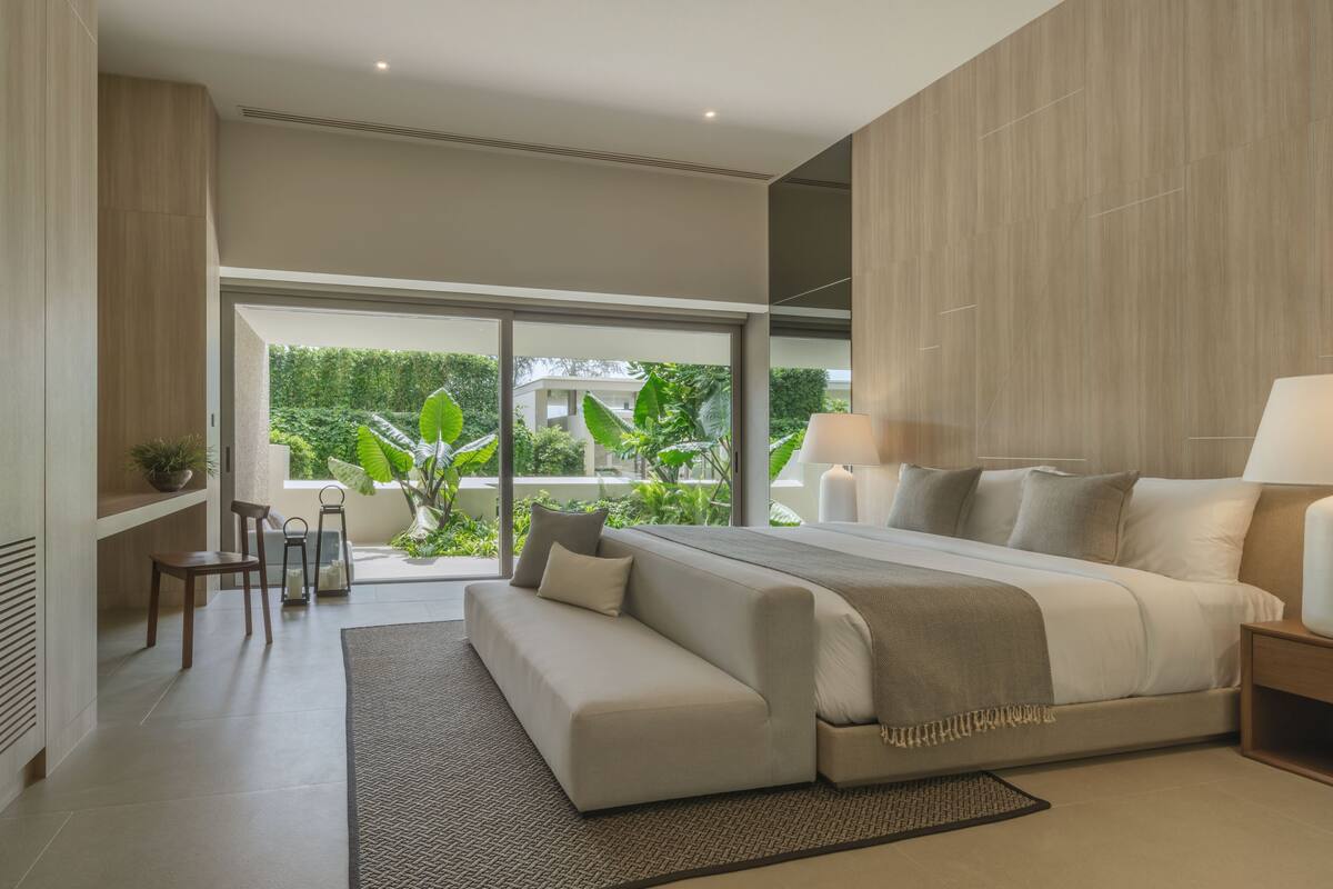 A modern bedroom with a large bed, a sofa, and a view of greenery outside.