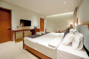 Une chambre bien éclairée, dotée d’un grand lit, d’un téléviseur à écran plat fixé au mur, d’un bureau avec une chaise et d’une porte.