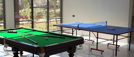 A pool table and a ping pong table in a room with large windows.