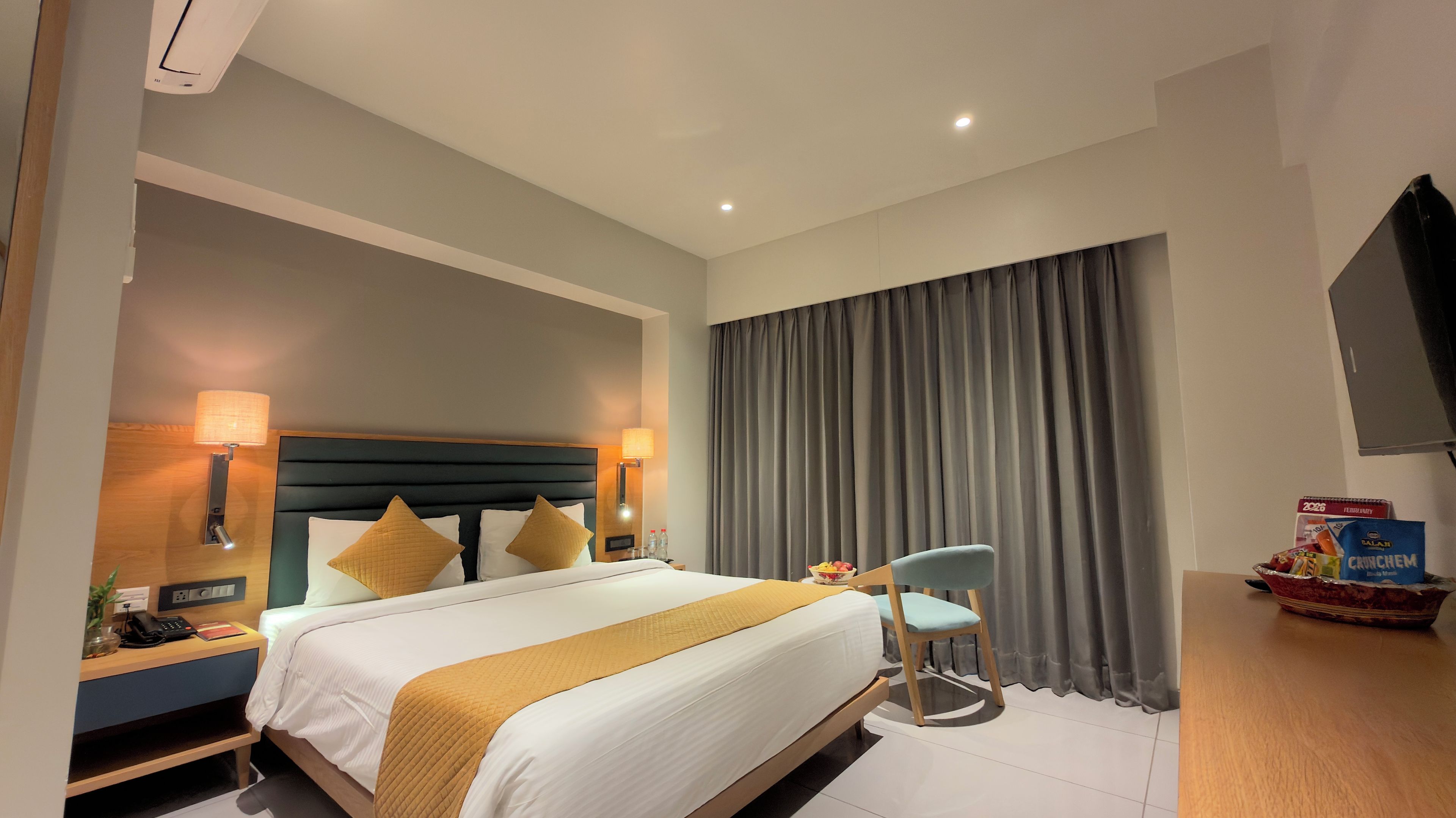 A hotel room with a bed, bedside lamps, a desk, a chair, a TV, and a window with curtains.