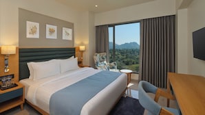 A hotel room with a large bed, a desk, a chair, and a view of the mountains.