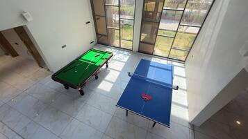 A room with a pool table, a ping pong table, and a window with a view of greenery.