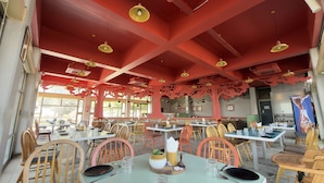 A restaurant with tables and chairs, red ceiling beams, and hanging pendant lights.