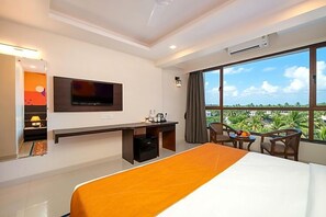 A hotel room with a bed, desk, TV, and a large window with a view. - Ira By Orchid Hotels , Porvorim (Alto de Porvorim)