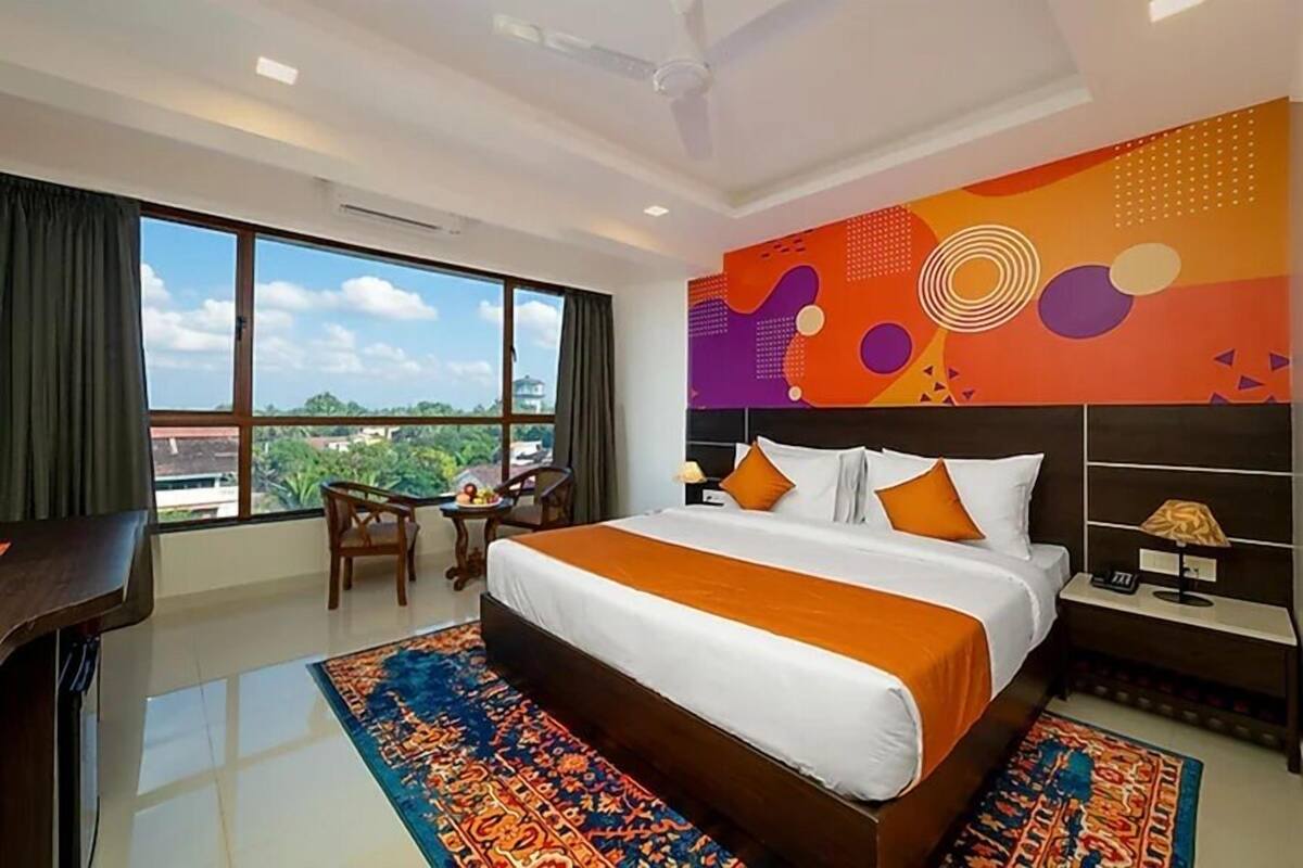 A hotel room with a large bed, a desk, a chair, a view of the city, and a colorful wall design.