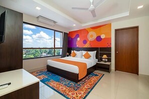Um quarto com cama, mesa de cabeceira, televisão, ventoinha no teto e uma janela grande.