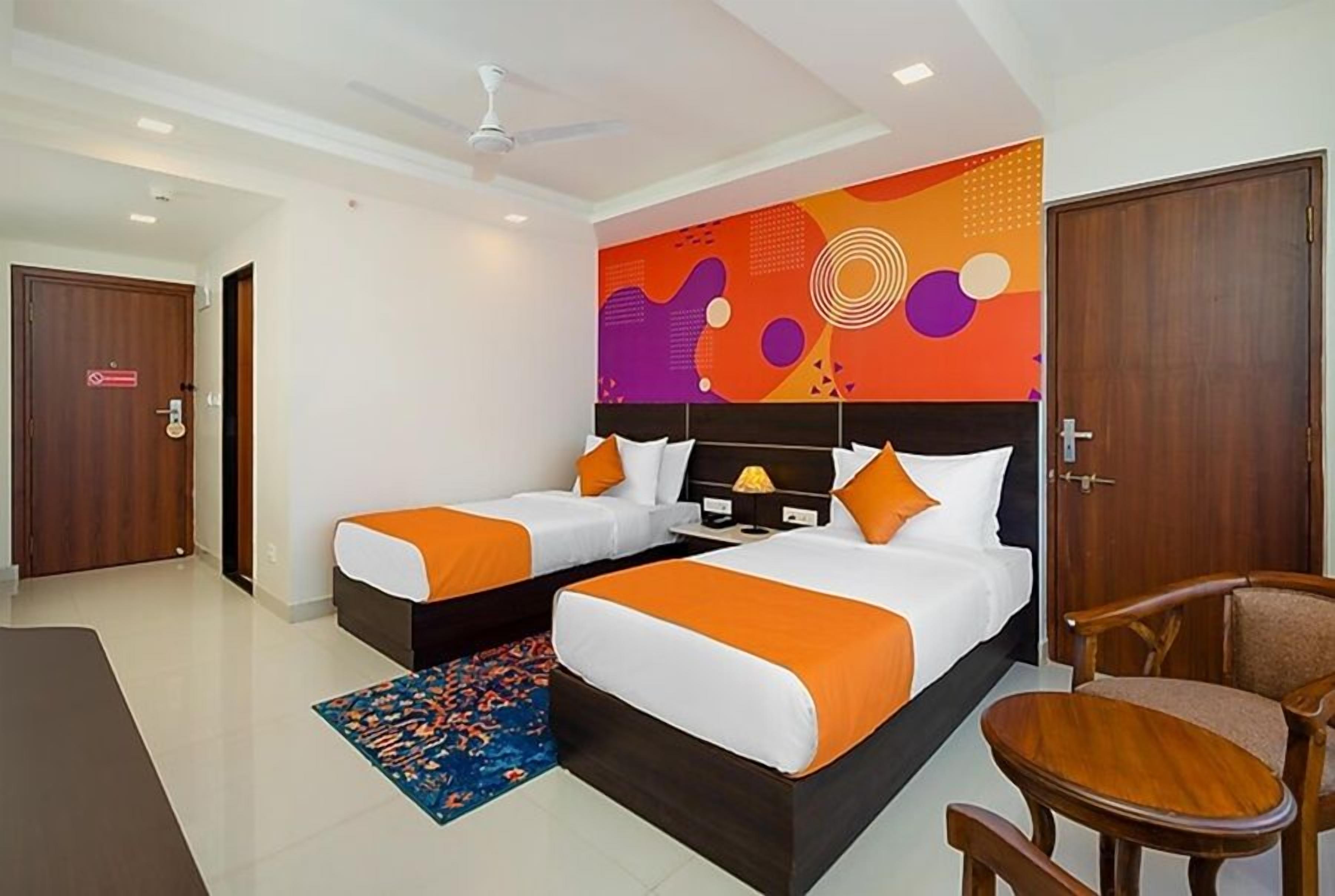 Habitación de hotel con dos camas, ventilador de techo, pared decorativa y una pequeña mesa con sillas.