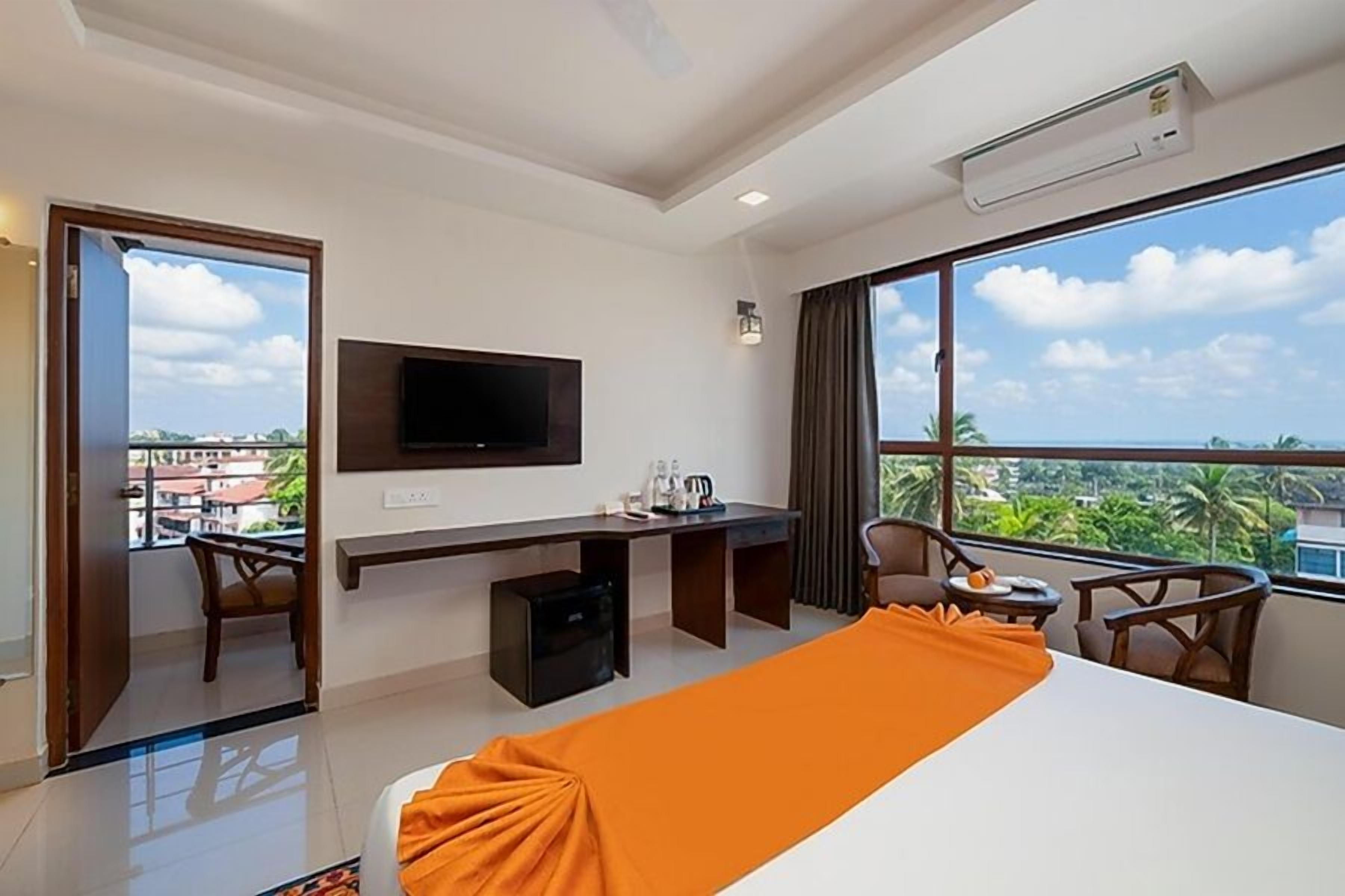 A hotel room with a bed, desk, chair, TV, and large windows with a view.
