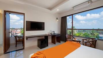 A hotel room with a bed, desk, chair, TV, and large windows with a view.