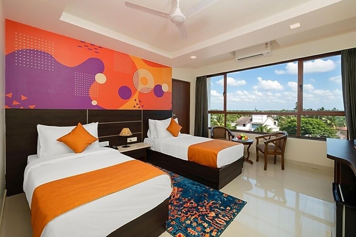 A hotel room with two beds, a desk, a chair, a large window with a view, and a ceiling fan.