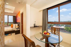A hotel room with a bed, a glass dining table with chairs, a small kitchen area, and a large window with a view. - Ira By Orchid Hotels , Porvorim (Alto de Porvorim)