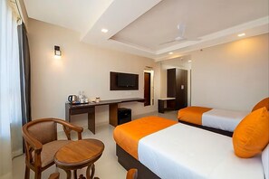Quarto de hotel com cama, duas mesas de cabeceira, escrivaninha com cadeira, televisão e ventilador de teto.