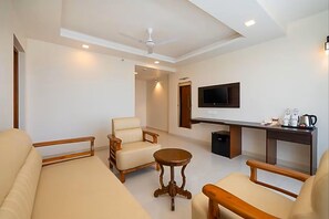 A hotel room with a sofa, armchairs, a small round table, a TV mounted on the wall, and a desk with a coffee maker. - Ira By Orchid Hotels , Porvorim (Alto de Porvorim)